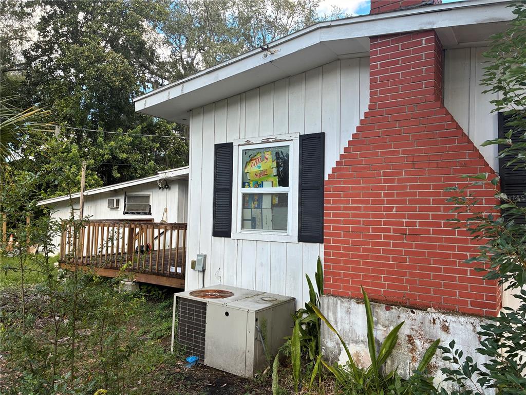 Exterior view of a house with white vertical siding, a red brick chimney, and deck — 1905 EMMETT STREET, KISSIMMEE, FL