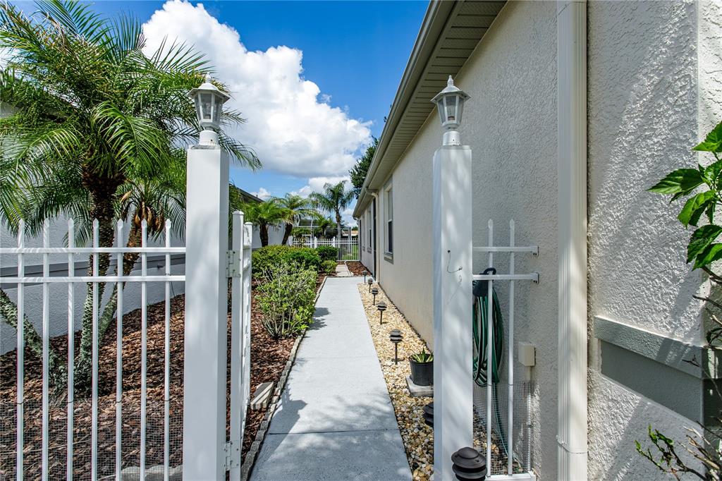A concrete walkway leads between a white fence and the side of a house — 8415 TAROCCO COURT, LAND O LAKES, FL