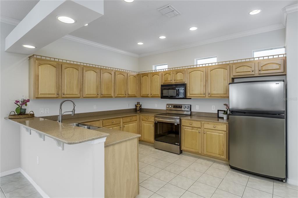 A kitchen with light wood cabinets, granite countertops, stainless steel appliances, and tile flooring — 8415 TAROCCO COURT, LAND O LAKES, FL