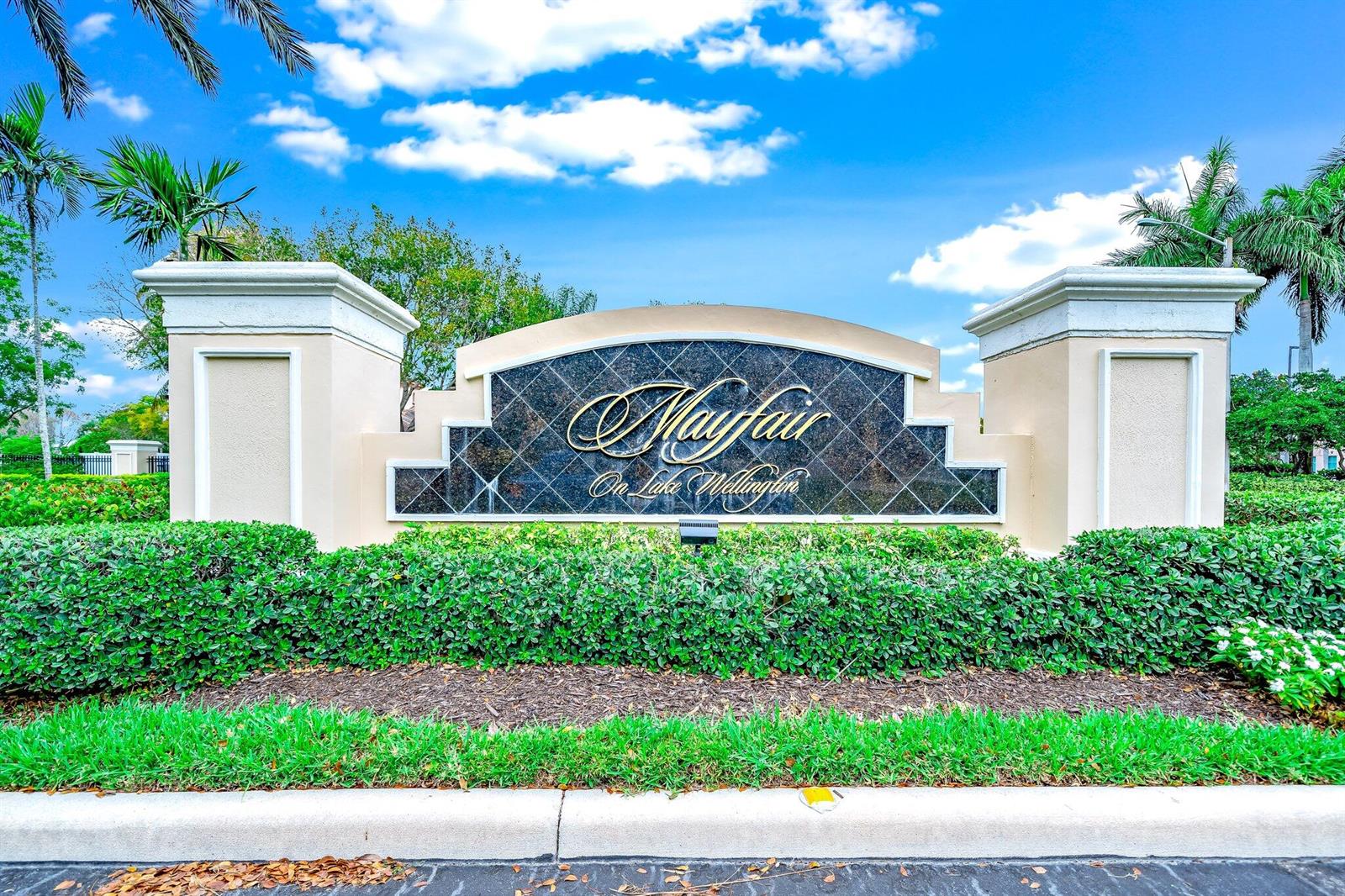 A stone monument sign for Mayfair on Lake Wellington sits behind a manicured hedge — 2106 Wingate Bend, Wellington FL 33414, WELLINGTON, FL