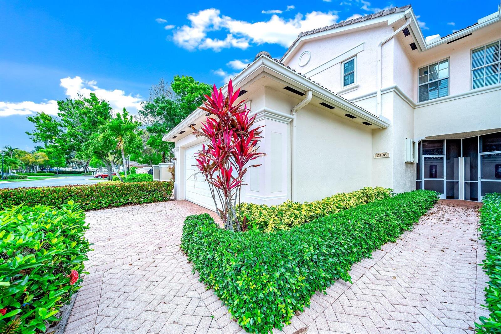 A two-story house exterior features a paved driveway, a red-leafed plant, and manicured hedges — 2106 Wingate Bend, Wellington FL 33414, WELLINGTON, FL
