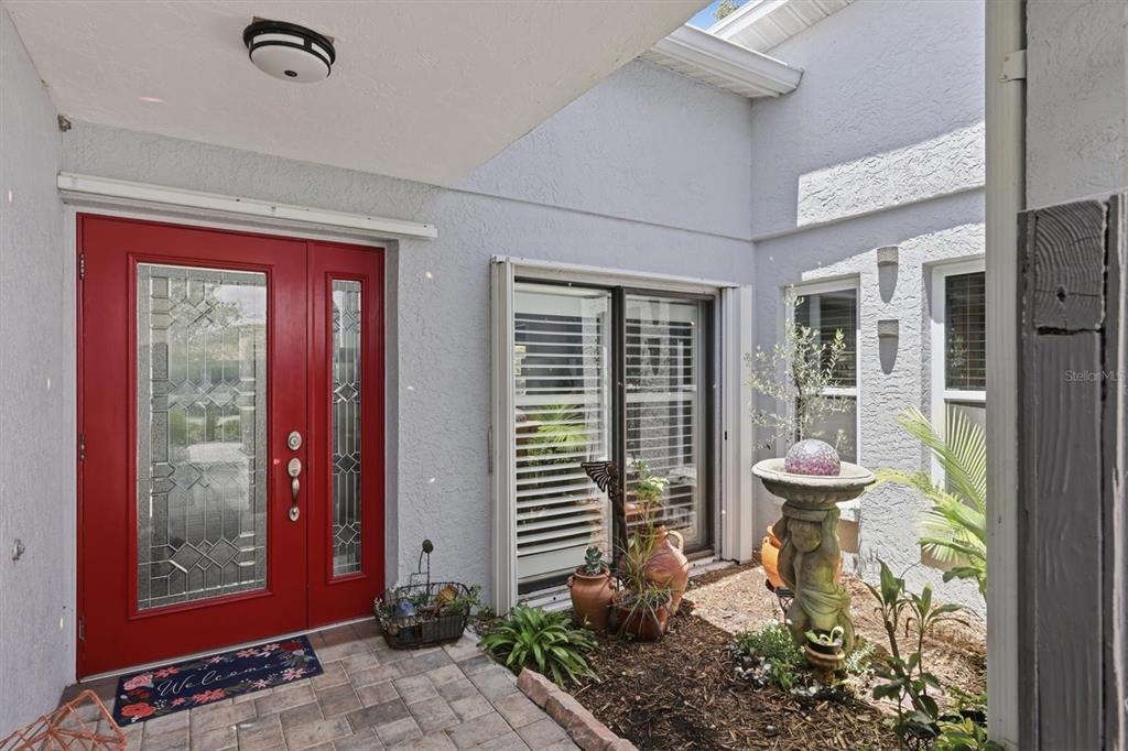 A red front door opens onto a paved entryway with a small garden and fountain — 3828 EASTON STREET, SARASOTA, FL