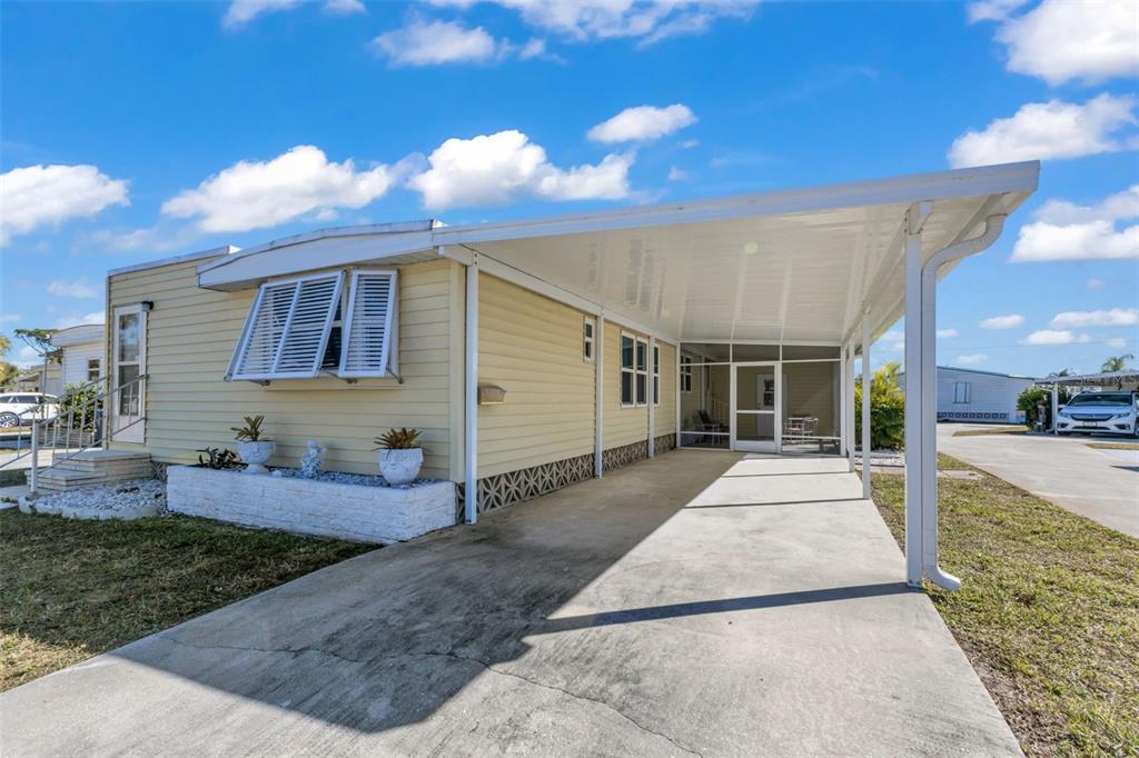 A yellow mobile home features a concrete driveway, a covered carport, and a screened-in porch — 1891 ENGLEWOOD ROAD UNIT 119, ENGLEWOOD, FL