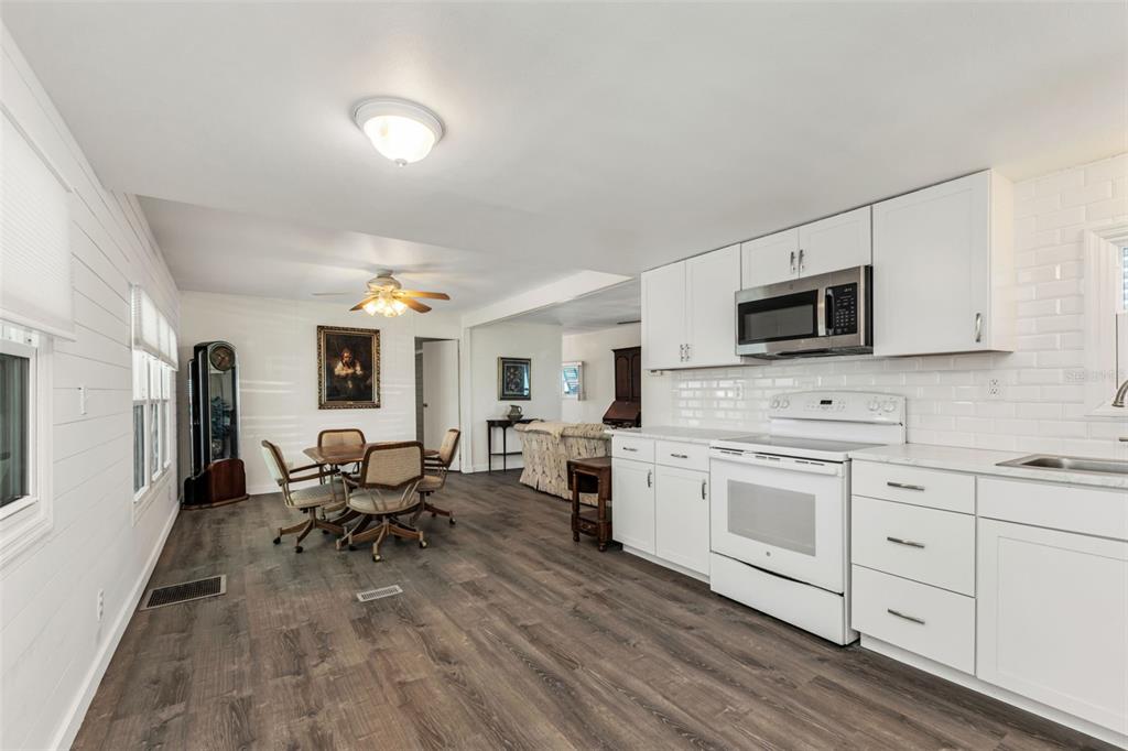 An open-concept kitchen and dining area with white cabinets, wood-look flooring, and white shiplap walls — 1891 ENGLEWOOD ROAD UNIT 119, ENGLEWOOD, FL