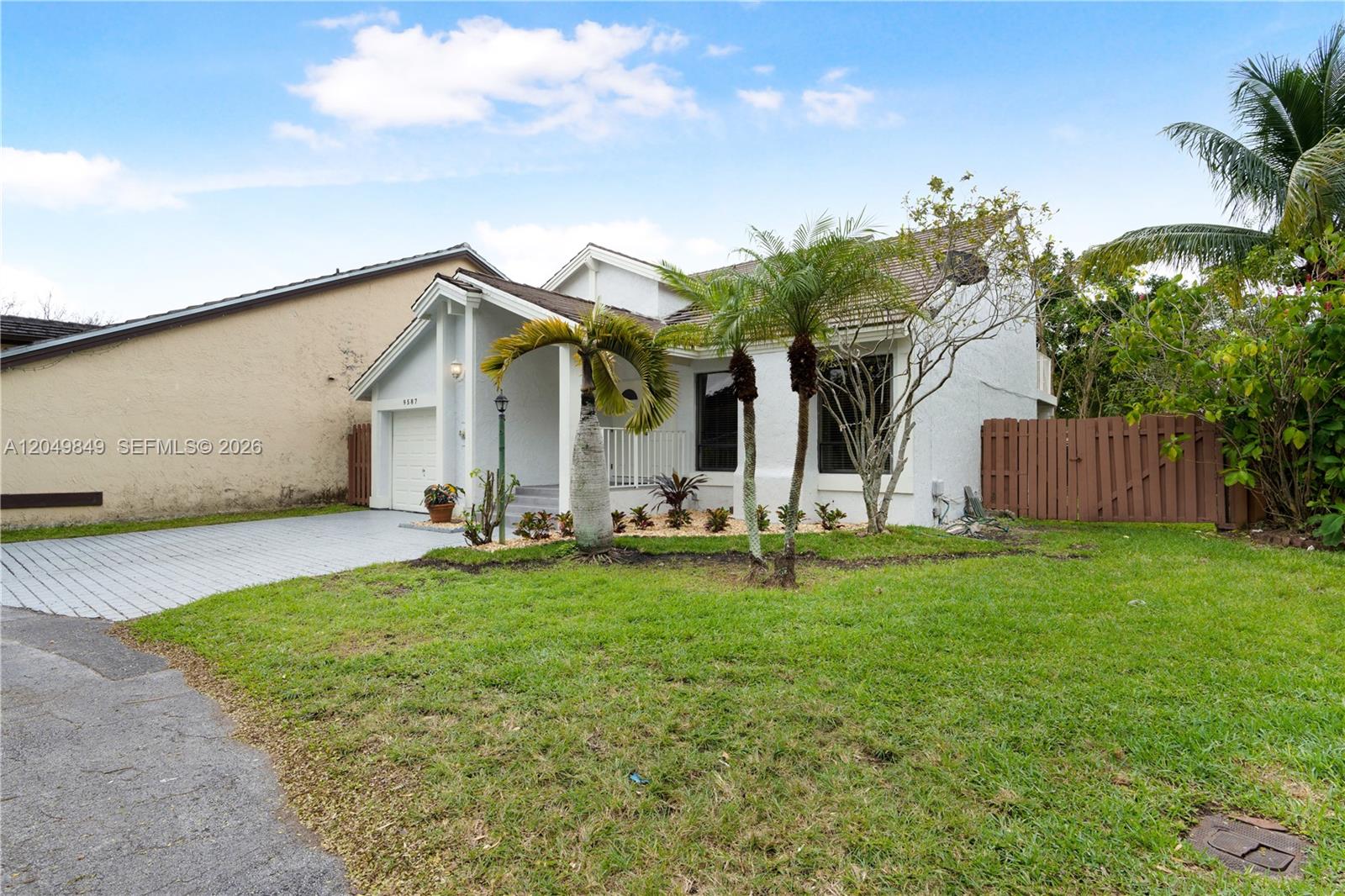 A single-story white house with a paved driveway, palm trees, and a wooden fence — 9587 SW 148th Ave Cir S, Miami FL 33196, MIAMI, FL