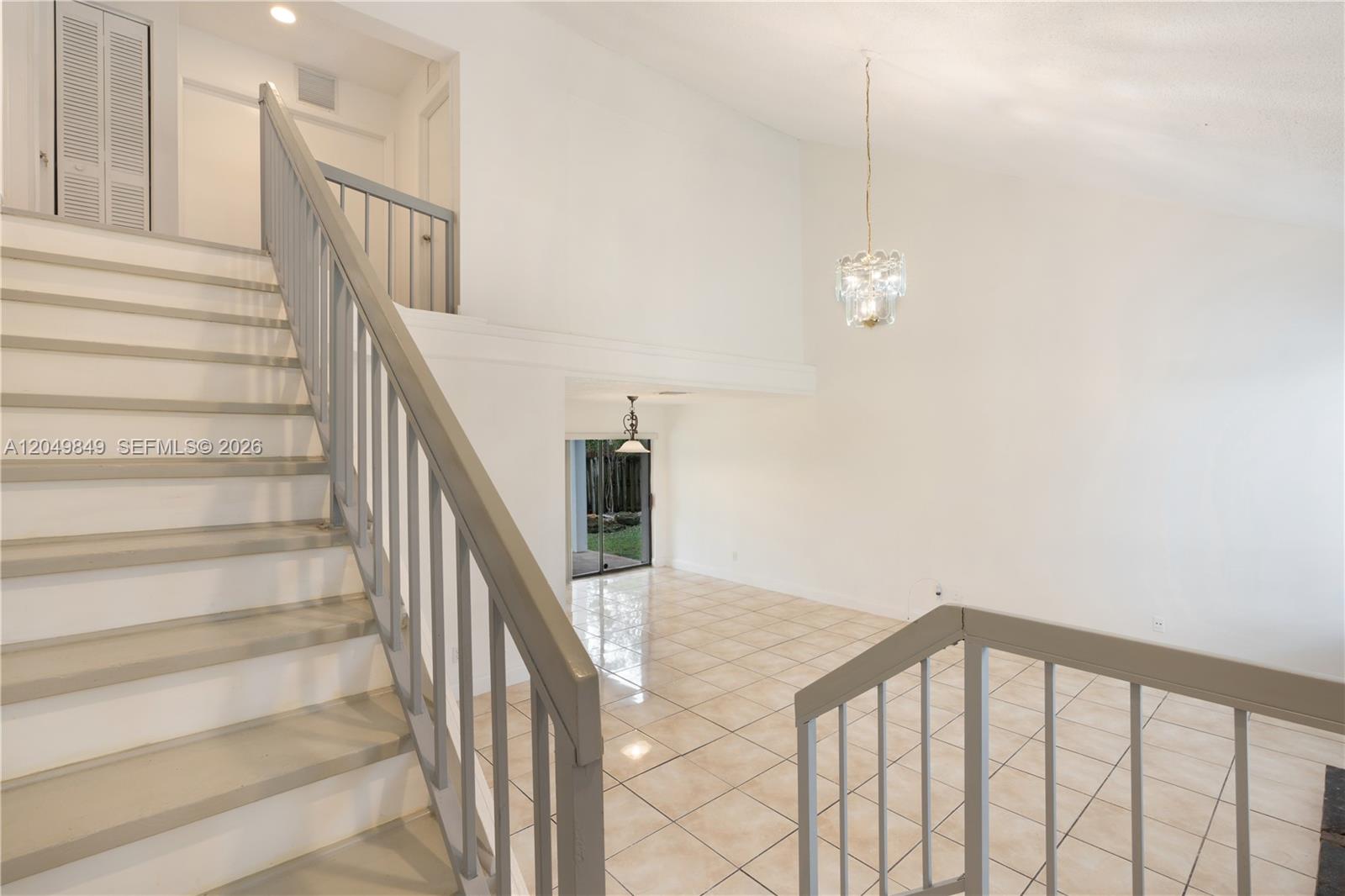 A staircase with gray railings leads down to a tiled living area with a chandelier — 9587 SW 148th Ave Cir S, Miami FL 33196, MIAMI, FL