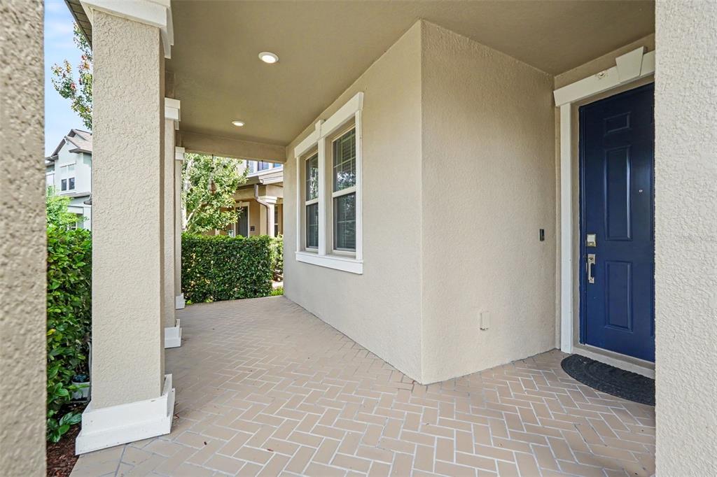 A covered front porch features a herringbone-patterned brick floor and a dark blue front door — 9173 SHADYSIDE LN, LAND O LAKES, FL