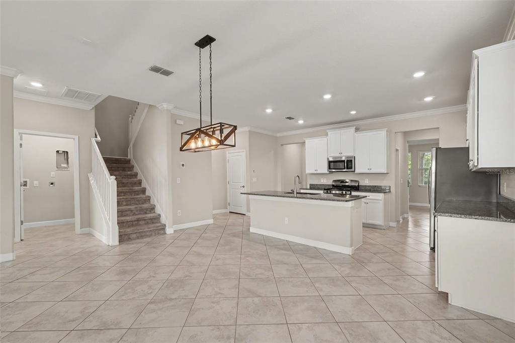 An open-concept kitchen and dining area features tile flooring, white cabinets, and a staircase — 9173 SHADYSIDE LN, LAND O LAKES, FL
