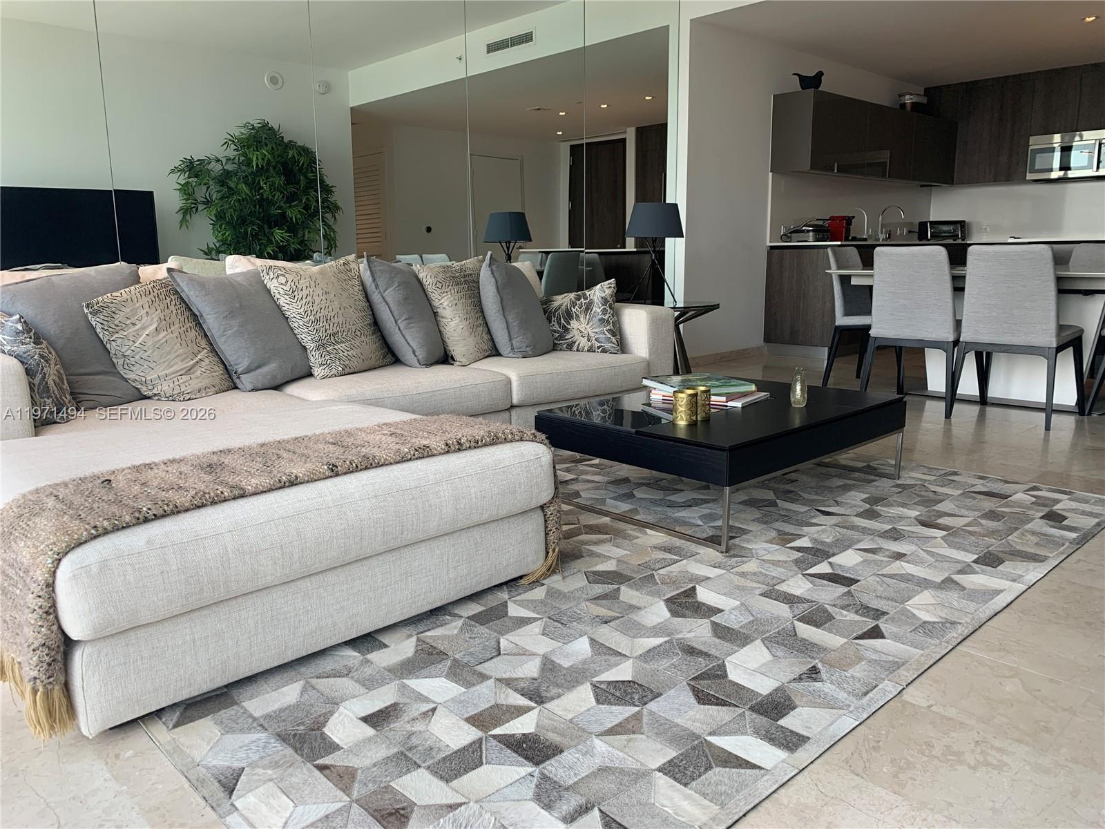 A modern living room features a large sectional sofa, a geometric rug, and an open kitchen — 68 SE 6th St # 3010, Miami FL 33131, MIAMI, FL