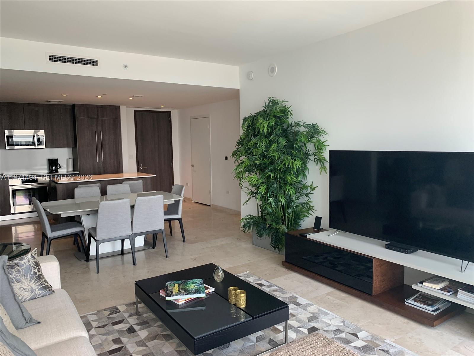 A modern living room features a large television, dining area, and kitchen with dark cabinetry — 68 SE 6th St # 3010, Miami FL 33131, MIAMI, FL