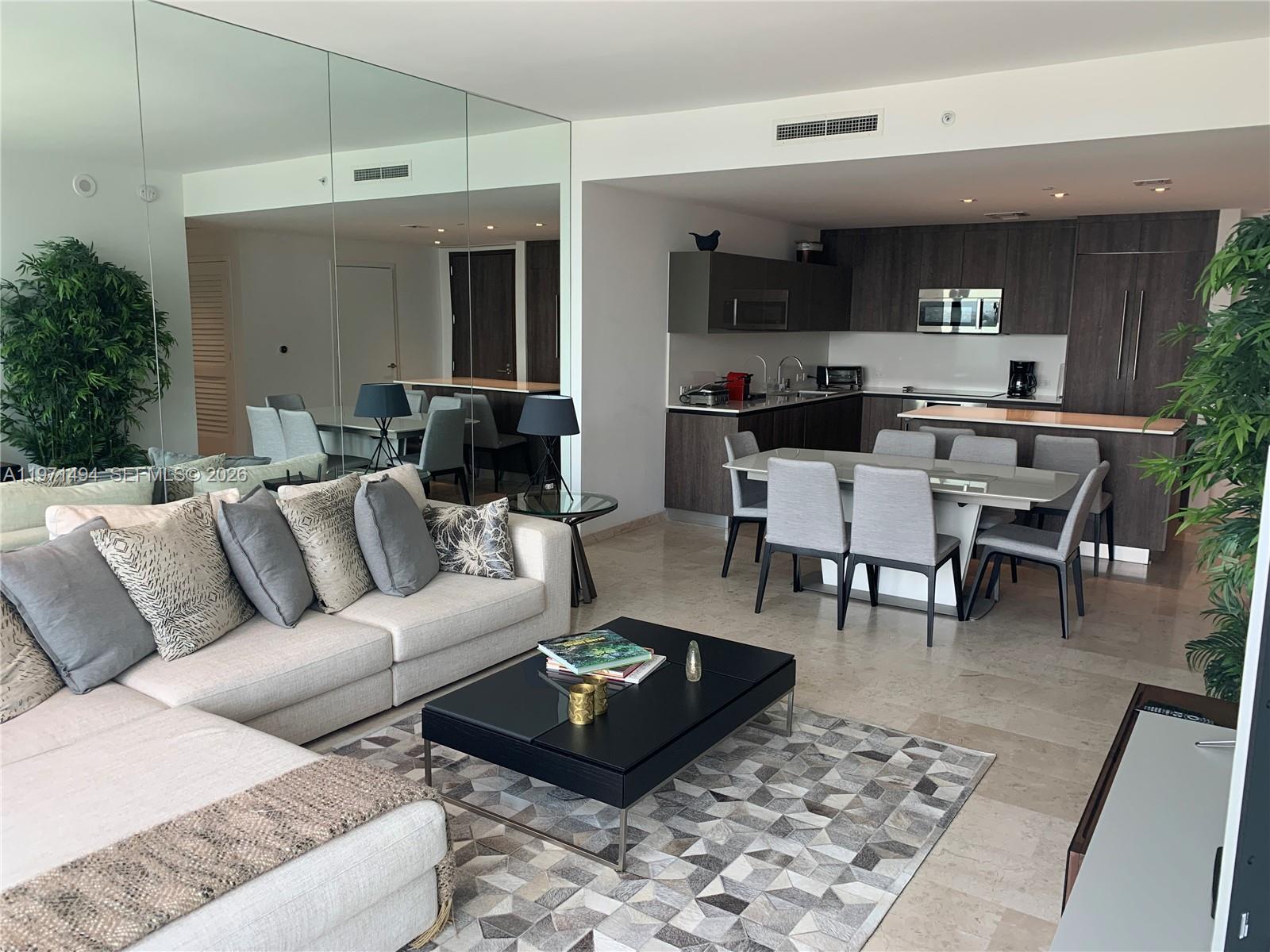 A modern open-concept living and dining area features a sectional sofa, dining set, and kitchen — 68 SE 6th St # 3010, Miami FL 33131, MIAMI, FL