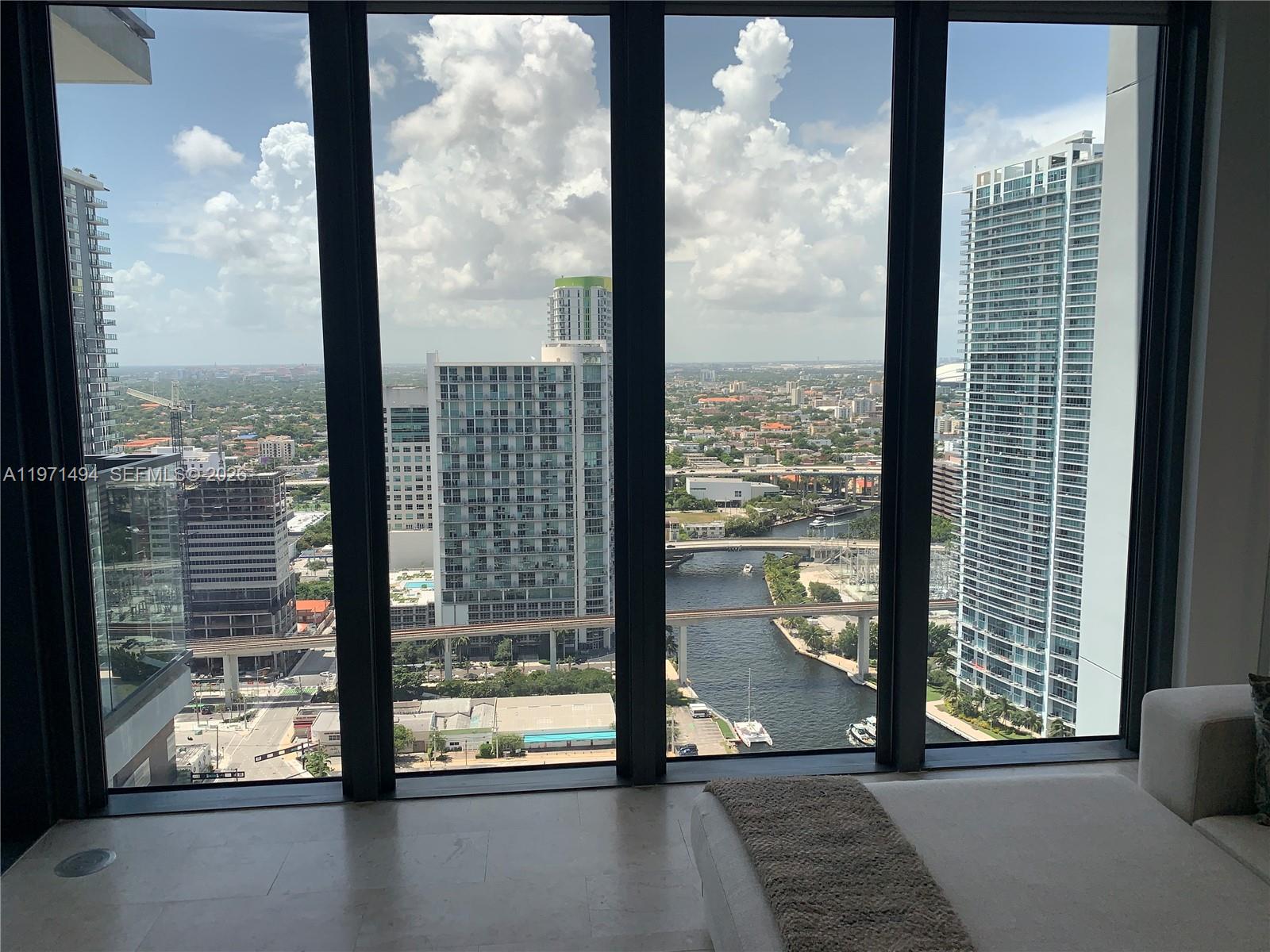 A view of a city skyline and river from a room with floor-to-ceiling windows — 68 SE 6th St # 3010, Miami FL 33131, MIAMI, FL