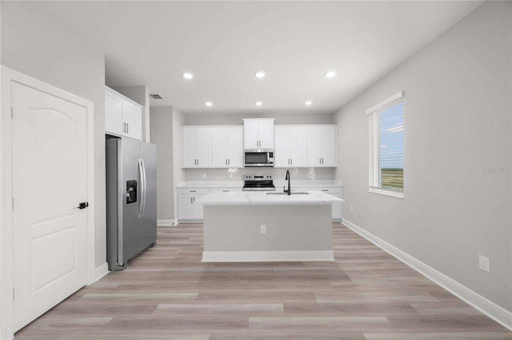 A modern kitchen features white cabinetry, stainless steel appliances, a center island, and wood-look flooring — 819 PONKAN COURT, BABSON PARK, FL