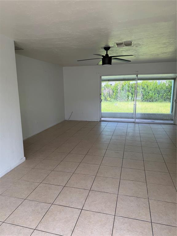 A room with beige tile flooring, a ceiling fan, and sliding glass doors to a yard — 21077 GERTRUDE AVENUE, PORT CHARLOTTE, FL
