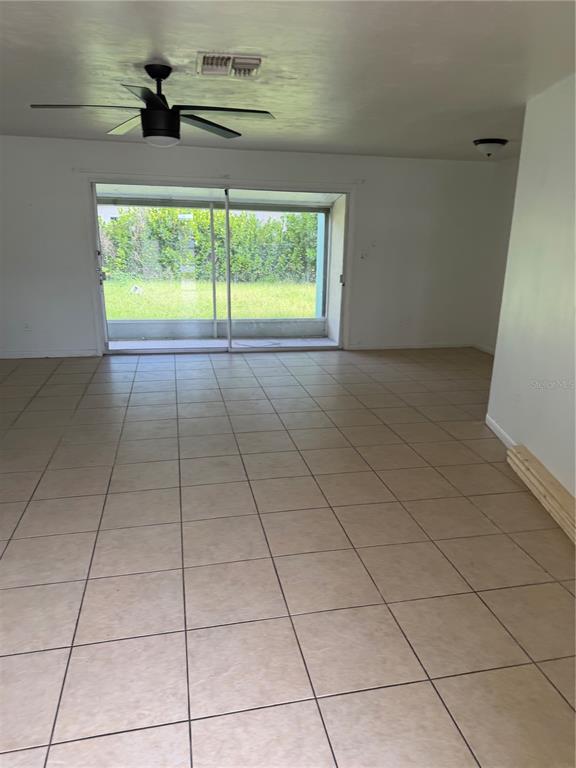 An empty room features beige tile flooring, a ceiling fan, and sliding glass doors — 21077 GERTRUDE AVENUE, PORT CHARLOTTE, FL