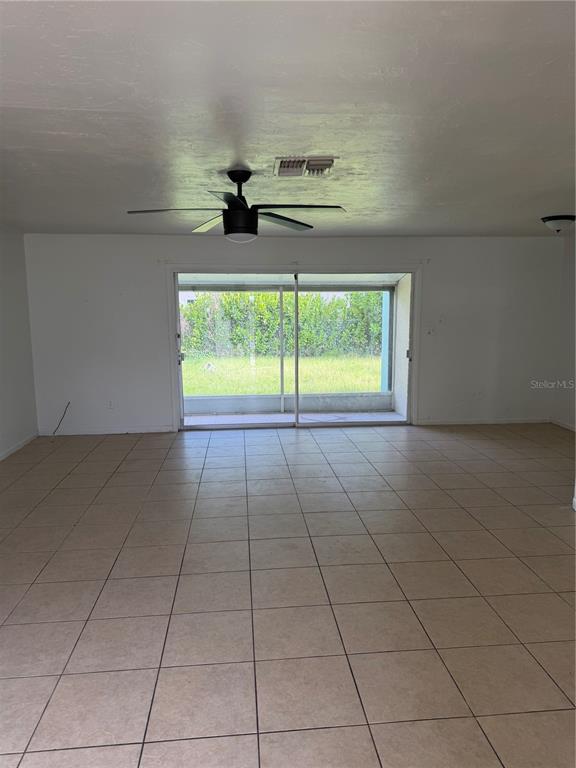 A spacious room with beige tile flooring, a ceiling fan, and sliding glass doors — 21077 GERTRUDE AVENUE, PORT CHARLOTTE, FL