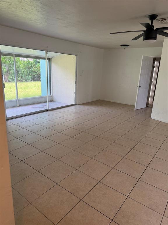 A room with light-colored tile flooring, a ceiling fan, and sliding glass doors to a patio — 21077 GERTRUDE AVENUE, PORT CHARLOTTE, FL