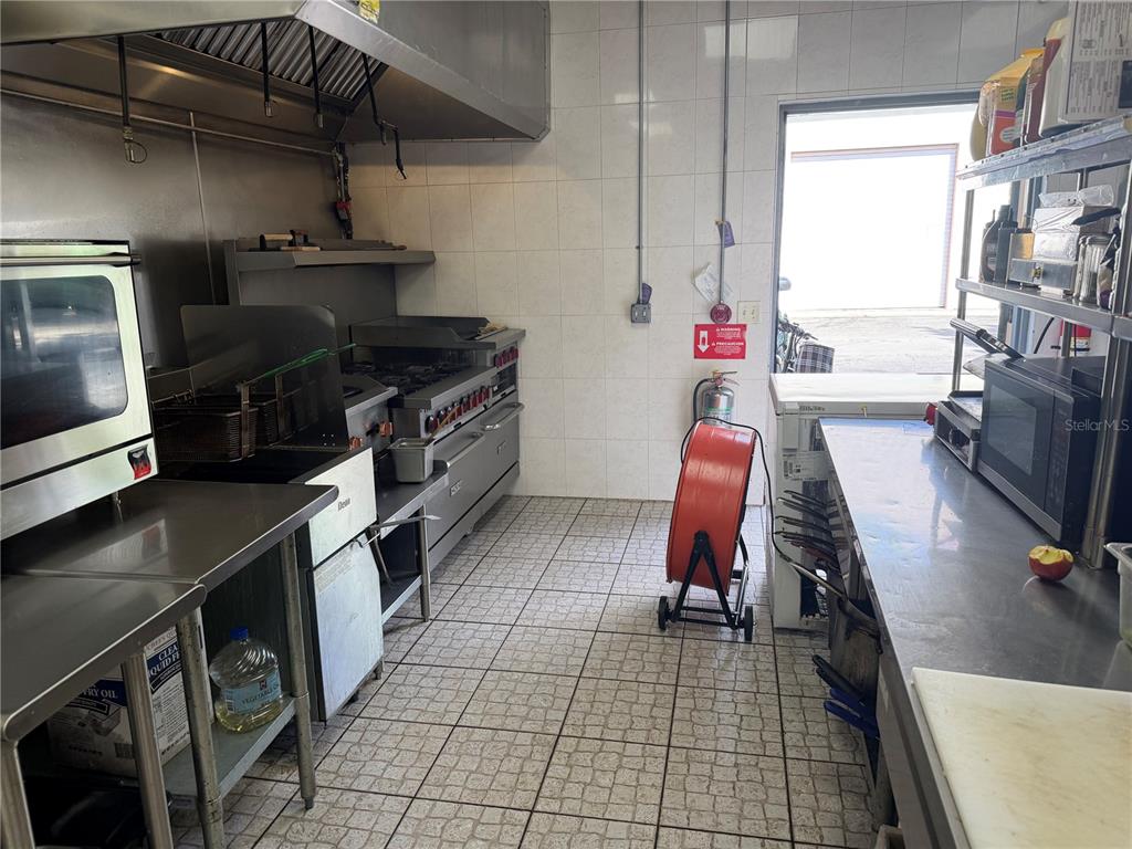 A commercial kitchen features stainless steel appliances, tiled walls, and a floor-mounted industrial fan — 9 NE PALM HARBOR VILLAGE WAY NE UNIT G, PALM COAST, FL
