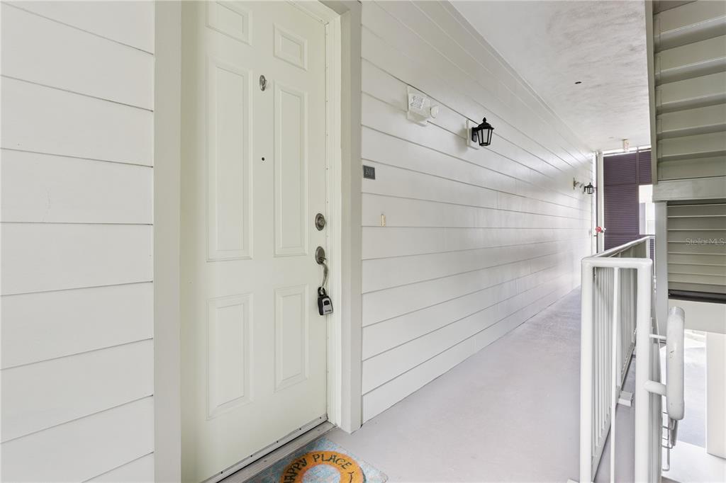A white exterior door with a lockbox leads to a covered apartment building walkway — 762 CELEBRATION AVENUE UNIT 2201, CELEBRATION, FL