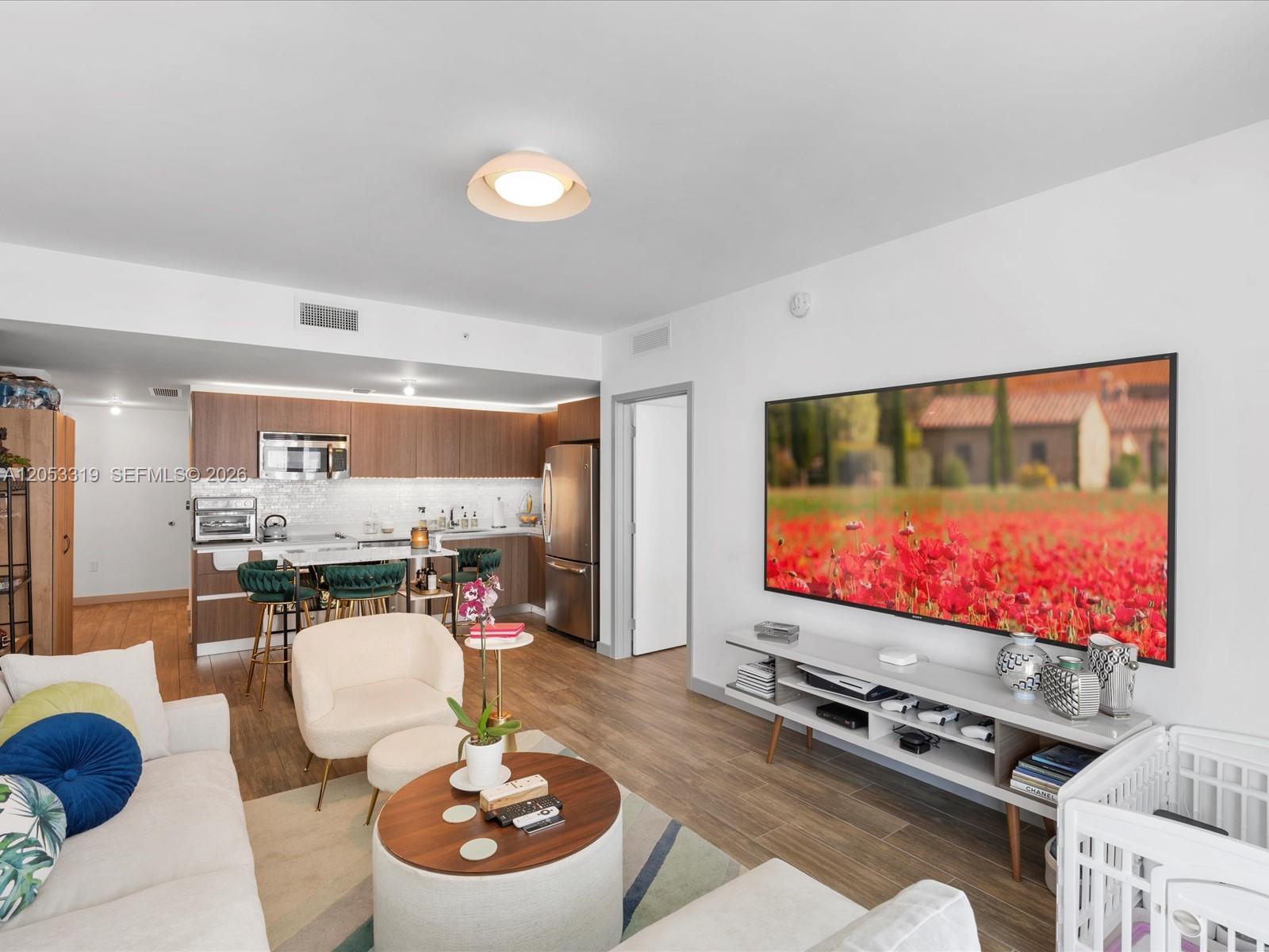 A modern living room with wood-look flooring, a large wall-mounted television, and an open kitchen — 1600 SW 1st Ave # 714, Miami FL 33129, MIAMI, FL