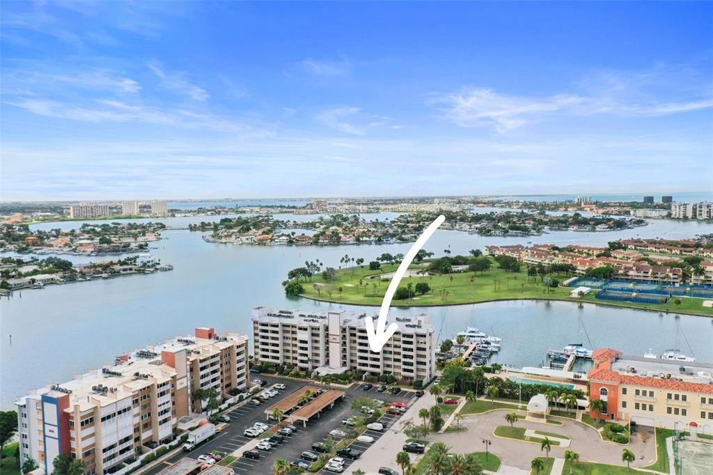 An aerial view shows a multi-story apartment building with a parking lot and marina — 450 TREASURE ISLAND CAUSEWAY UNIT 502, TREASURE ISLAND, FL
