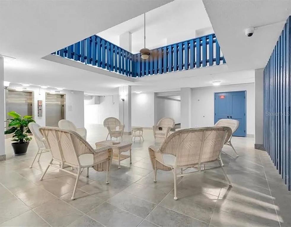A bright lobby area features wicker furniture, tile flooring, and a blue railed atrium opening — 450 TREASURE ISLAND CAUSEWAY UNIT 502, TREASURE ISLAND, FL