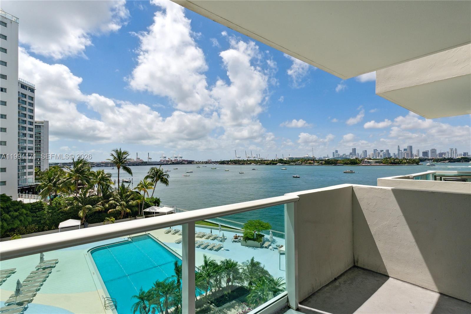 A balcony overlooks a swimming pool, palm trees, a bay, and a distant city skyline — 1200 West Ave # 528, Miami Beach FL 33139, MIAMI BEACH, FL