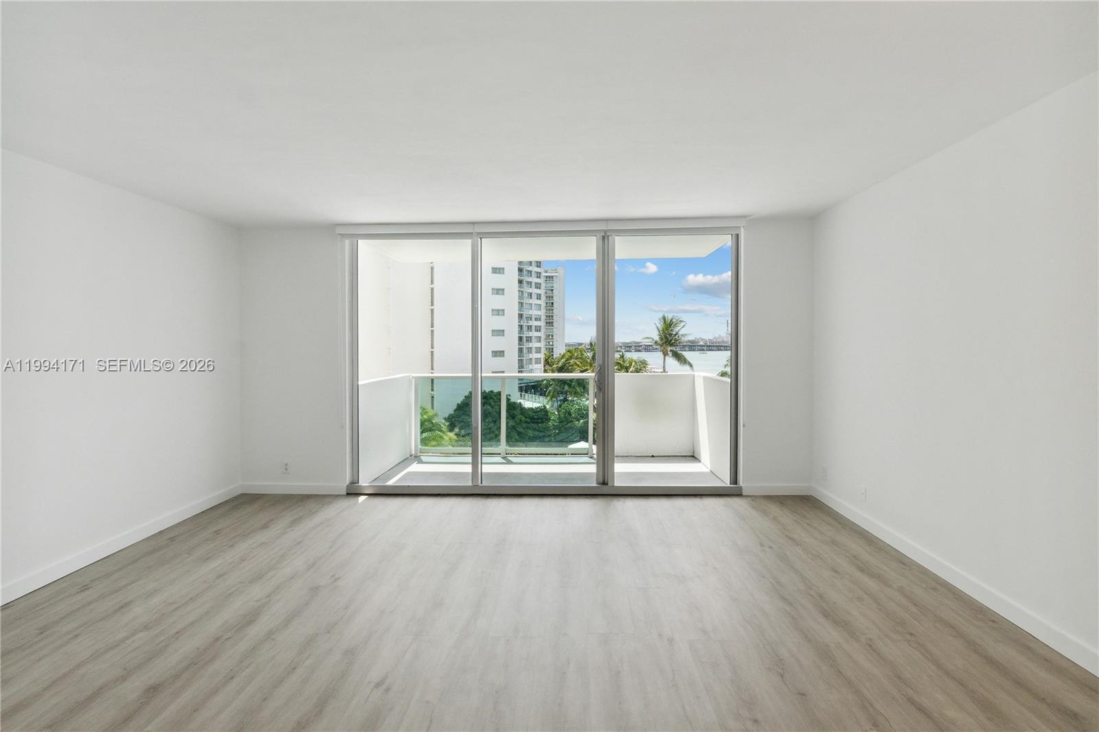 An empty room with light wood-look flooring features a large sliding glass door to a balcony — 1200 West Ave # 528, Miami Beach FL 33139, MIAMI BEACH, FL