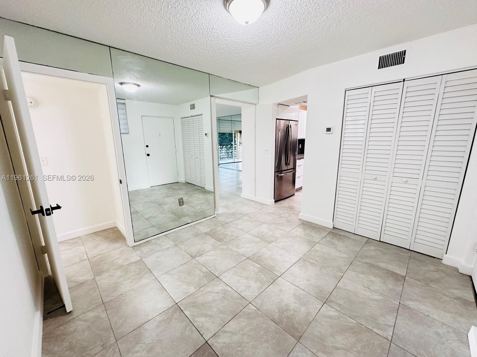 A tiled room features a mirrored wall, white louvered closet doors, and a kitchen view — 3490 Foxcroft Rd # B208, Miramar FL 33025, MIRAMAR, FL