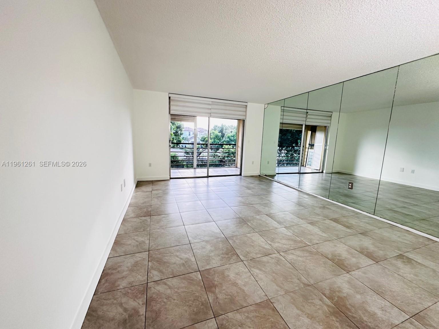 An empty room features large floor tiles, white walls, a mirrored wall, and a sliding door — 3490 Foxcroft Rd # B208, Miramar FL 33025, MIRAMAR, FL