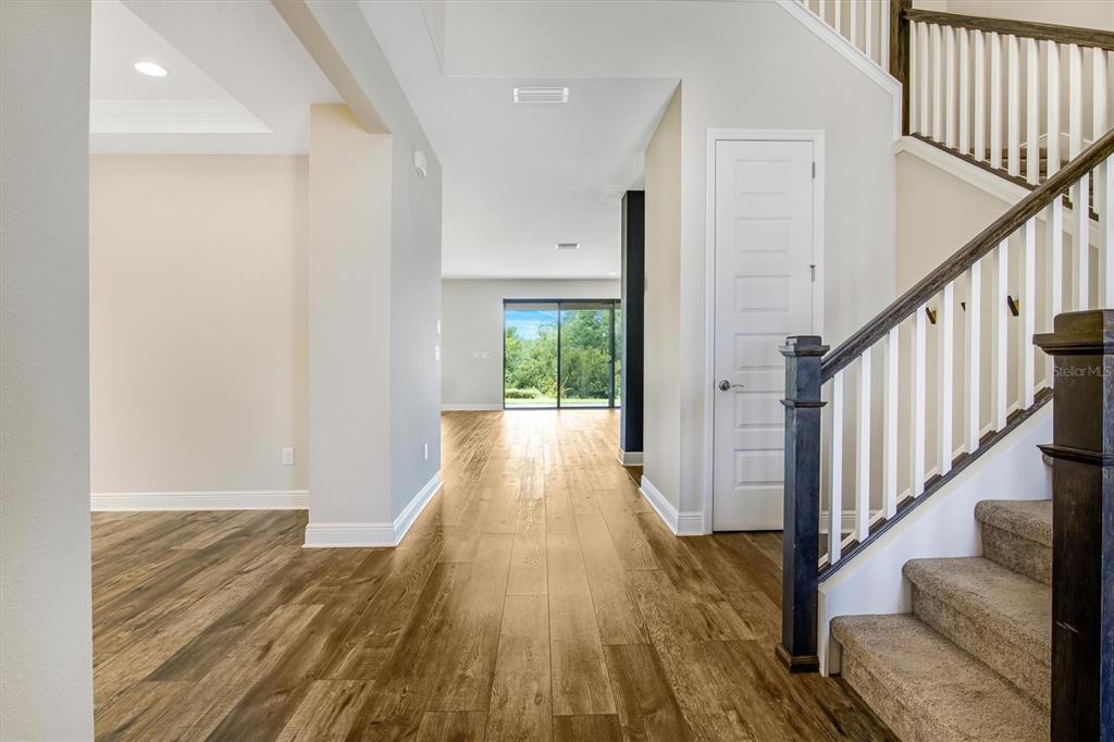 An entryway with wood flooring leads to a living area with sliding glass doors — 12859 SATIN LILY DRIVE, RIVERVIEW, FL