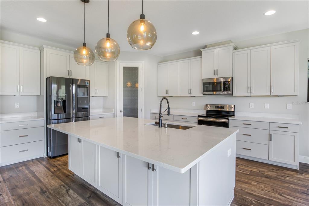 A modern kitchen features white cabinetry, a large quartz island, and dark wood flooring — 12859 SATIN LILY DRIVE, RIVERVIEW, FL
