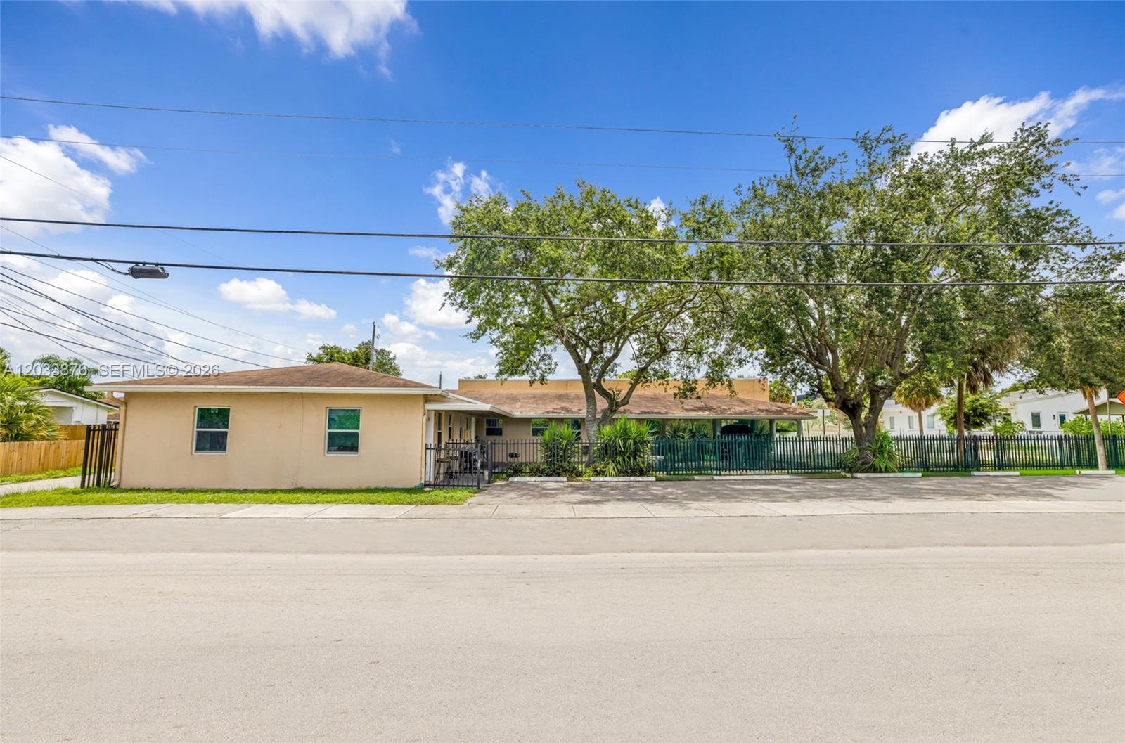 A single-story tan house with a fenced yard and large trees sits along a street — 2247 Simms St, Hollywood FL 33020, HOLLYWOOD, FL