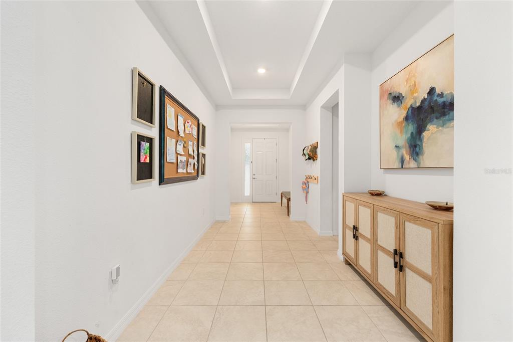 A bright hallway features tile flooring, a tray ceiling, a console table, and wall art — 7431 SW 65TH PLACE ROAD, OCALA, FL