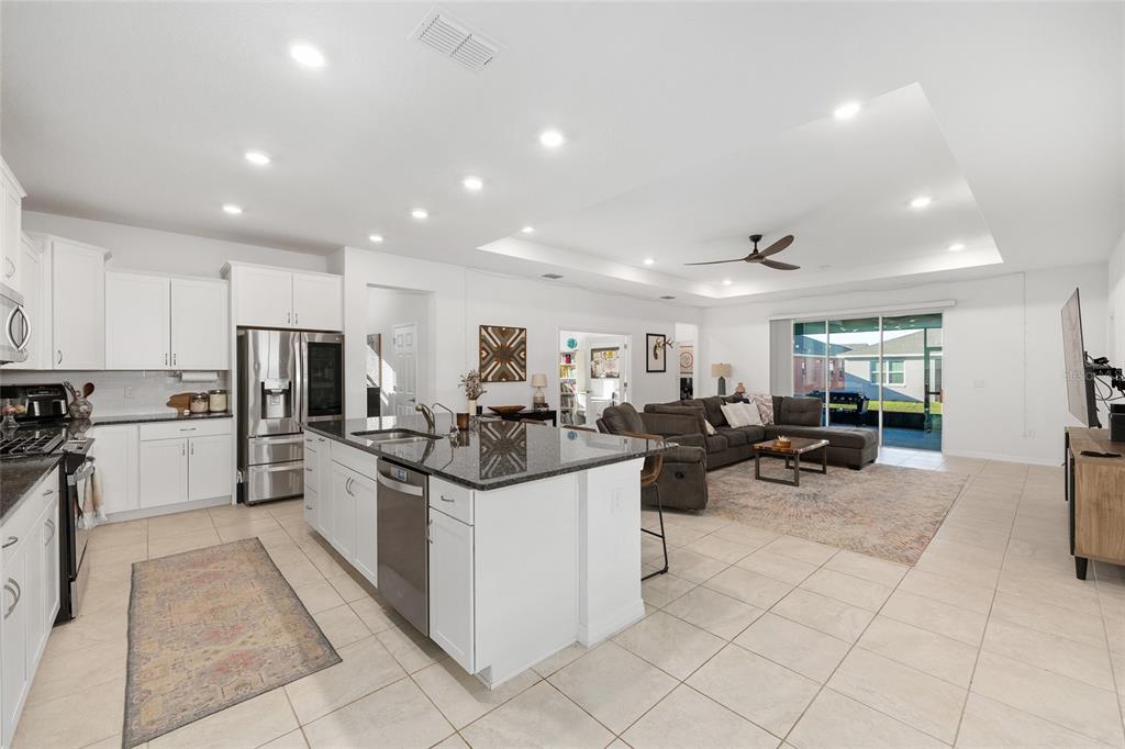 An open-concept kitchen with a granite island and white cabinets overlooks a living room area — 7431 SW 65TH PLACE ROAD, OCALA, FL
