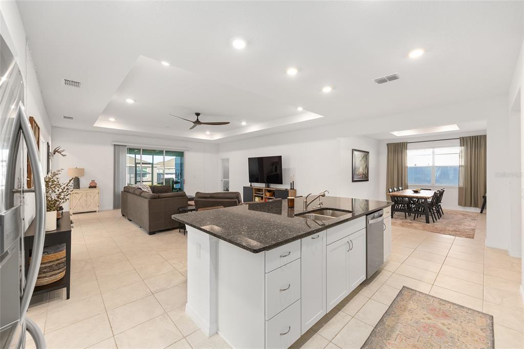 An open-concept kitchen with a granite island overlooks a living room and dining area — 7431 SW 65TH PLACE ROAD, OCALA, FL