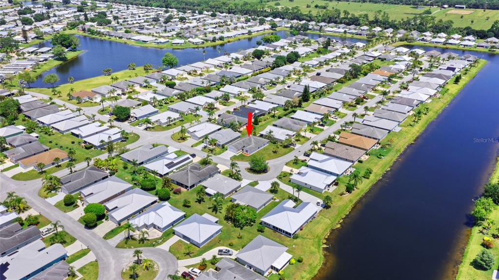 An aerial view shows a suburban neighborhood with houses surrounding a large retention pond — 6527 ALHELI, FORT PIERCE, FL