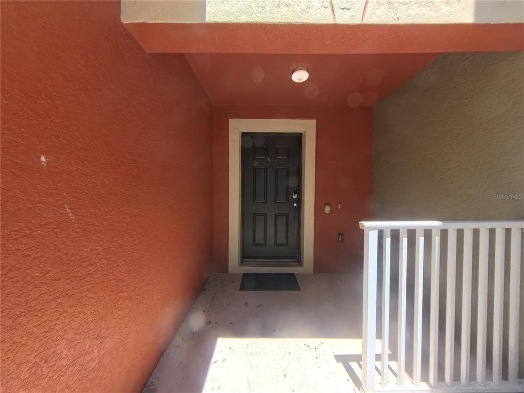 A covered entryway features a dark front door, a light fixture, and a white railing — 215 GLOWING PEACE LANE UNIT 86, ORLANDO, FL