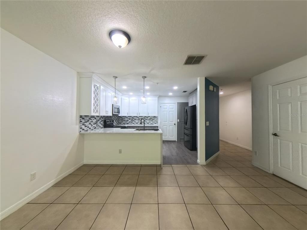A kitchen with white cabinets, a mosaic backsplash, and a breakfast bar overlooks a tiled room — 215 GLOWING PEACE LANE UNIT 86, ORLANDO, FL