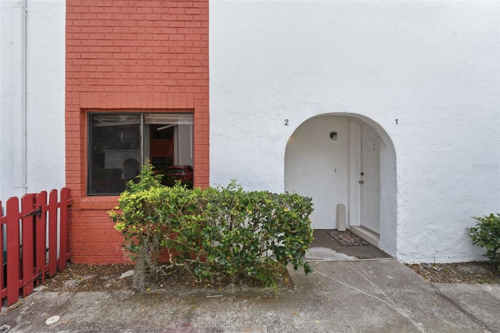 A white stucco building exterior features a red brick accent wall and an arched entryway — 910 BIG TREE ROAD UNIT 202, SOUTH DAYTONA, FL