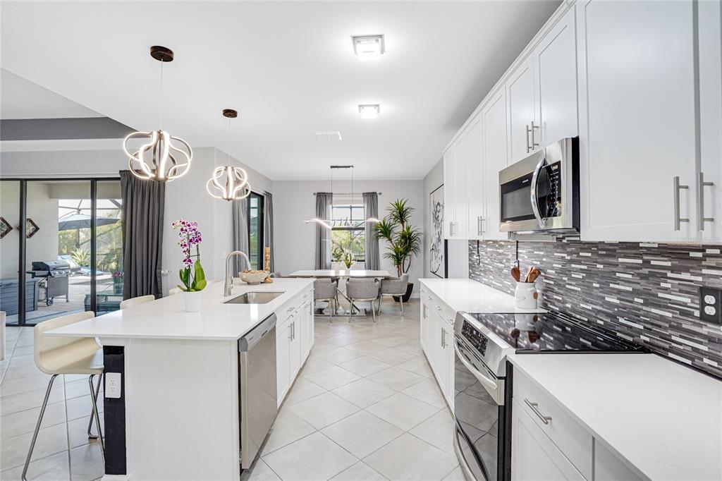 A modern kitchen features white cabinetry, a central island with a sink, and stainless appliances — 4970 OYSTER PEARL STREET, LAKEWOOD RANCH, FL