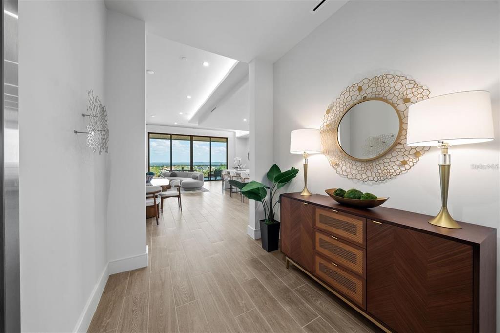 A modern entryway features a wood console table, gold-framed mirror, and lamps, leading to a living area — 1591 GULF OF MEXICO DRIVE UNIT 515, LONGBOAT KEY, FL