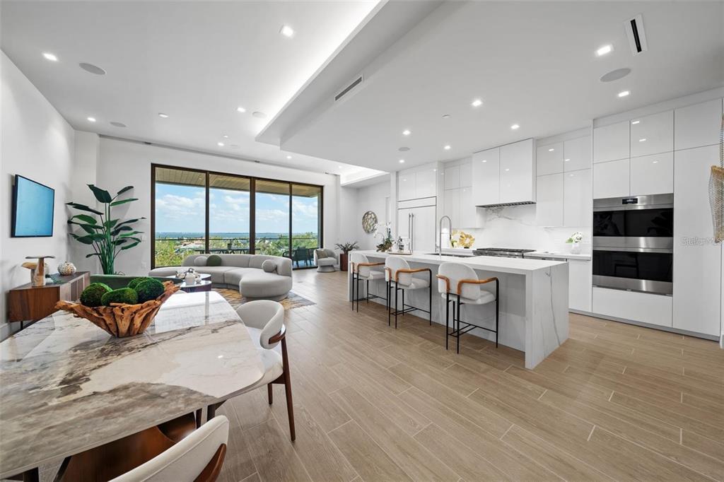 A modern open-concept kitchen and living area features white cabinetry, marble surfaces, and floor-to-ceiling windows — 1591 GULF OF MEXICO DRIVE UNIT 515, LONGBOAT KEY, FL
