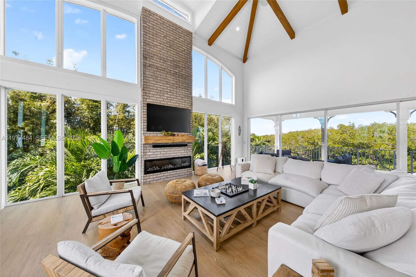 A bright living room features a brick fireplace, vaulted ceiling with beams, and floor-to-ceiling windows — 146 Mockingbird Rd, Tavernier FL 33070, TAVERNIER, FL