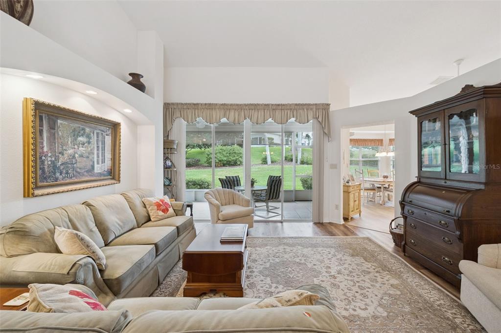A living room with a beige sofa, wooden coffee table, and sliding glass doors to a patio — 5000 SAWGRASS LAKE CIRCLE, LEESBURG, FL