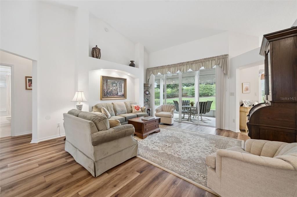 A living room with vaulted ceilings, wood-look flooring, and sliding glass doors to a patio — 5000 SAWGRASS LAKE CIRCLE, LEESBURG, FL