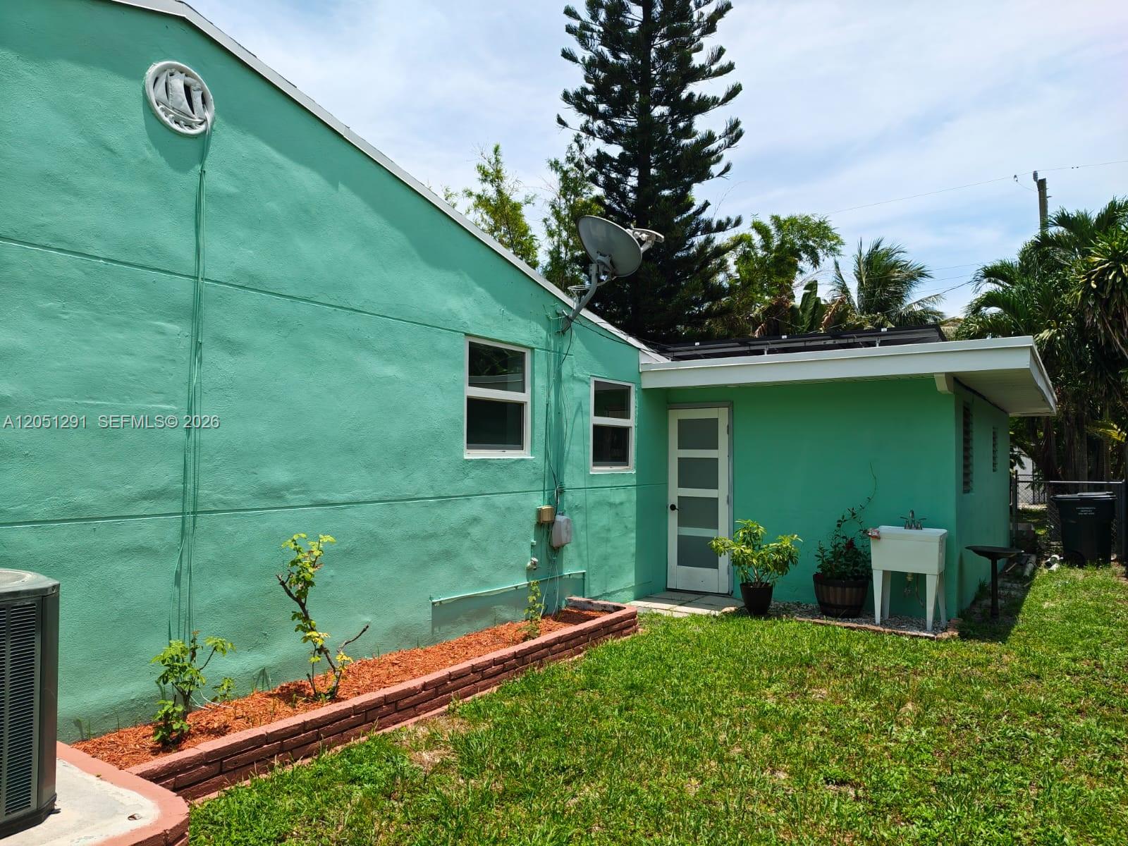The exterior of a teal-painted house features a brick planter, a utility sink, and windows — 2418 Scott St, Hollywood FL 33020, HOLLYWOOD, FL