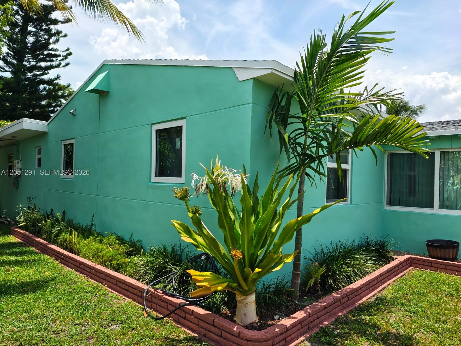 A turquoise house exterior features a brick-bordered garden bed with a large flowering plant — 2418 Scott St, Hollywood FL 33020, HOLLYWOOD, FL