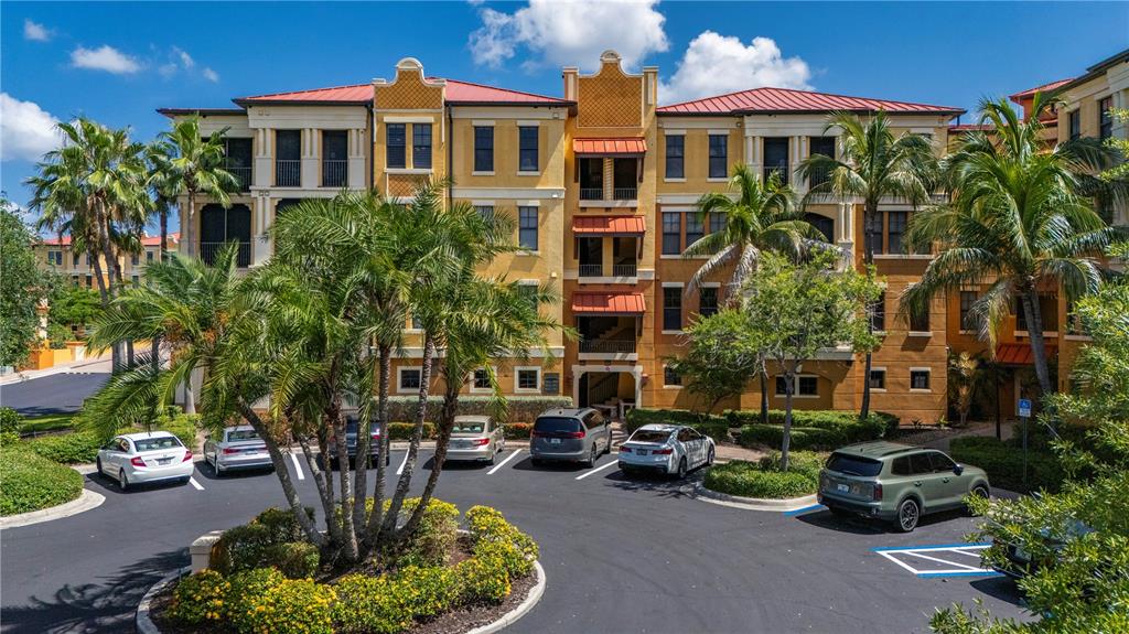 A multi-story yellow apartment building with a red roof stands behind a paved parking lot — 98 VIVANTE BOULEVARD UNIT 9844, PUNTA GORDA, FL