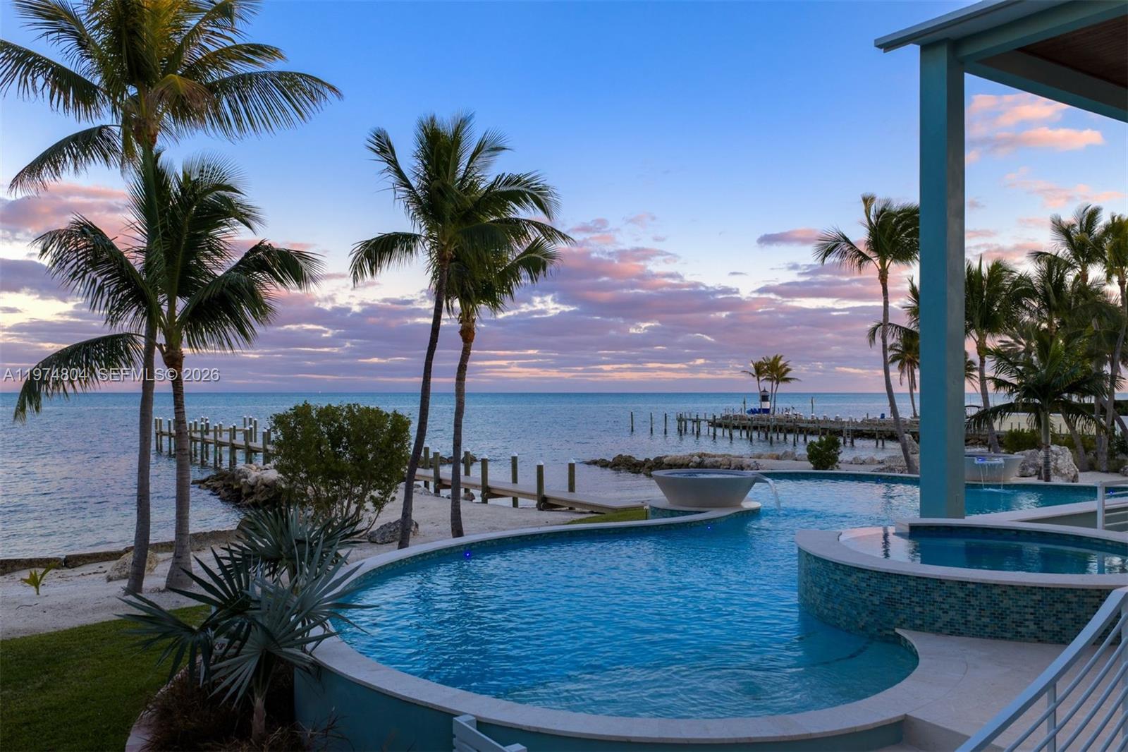 A curved infinity pool overlooks a sandy beach, wooden docks, and the ocean at sunset — 88351 Old Hwy, Islamorada FL 33070, ISLAMORADA, FL